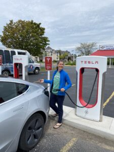 Woman holding a cord charges an electric vehicle at a Tesla supercharging station