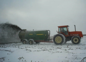 Tractor pulling a trailer full of manure spreads on a frozen snowy field