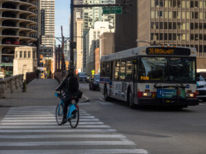 A Chicago Transit Authority bus drives down State Street past a cyclist and pedestrian in downtown Chicago