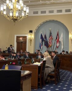 Congress people sit around wood tables in an ornamented room during the House Natural Resources Committee debate on reconciliation May 2025