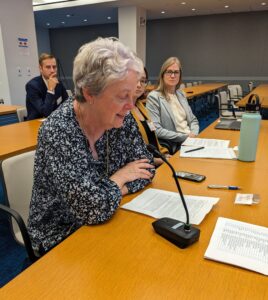 ELPC Senior Attorney Nancy Stoner sits at a large wooden table with other people, testifying into a microphone as she reads from a paper