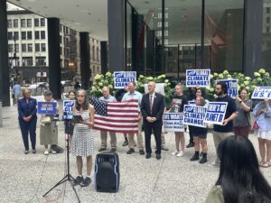 ELPC's Susan Mudd speaks into a microphone in front of a group of people holding an American flag and signs about protecting the environment at Chicago's Federal Plaza