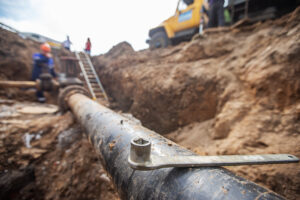 A construction crew works on a big pipe in the ground, surrounded by dirt