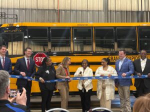 A group of Grand Rapids school and transportation officials cut a ribbon in front of an electric school bus